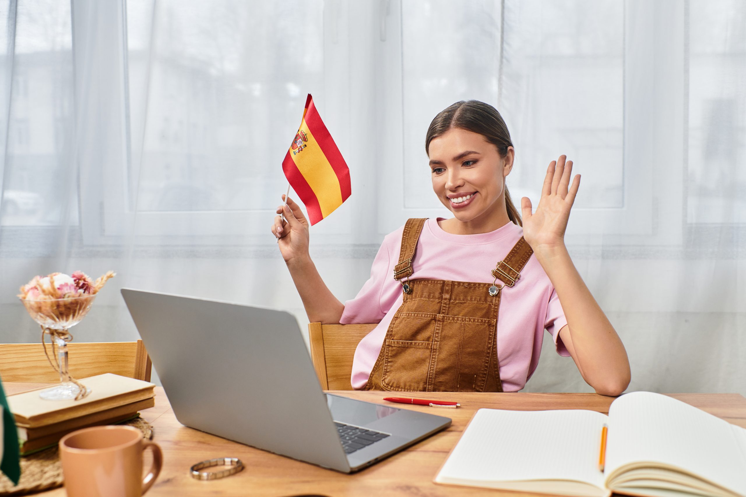 cheerful-young-woman-waving-while-engaging-virtual-conversation-with-spanish-flag-hand