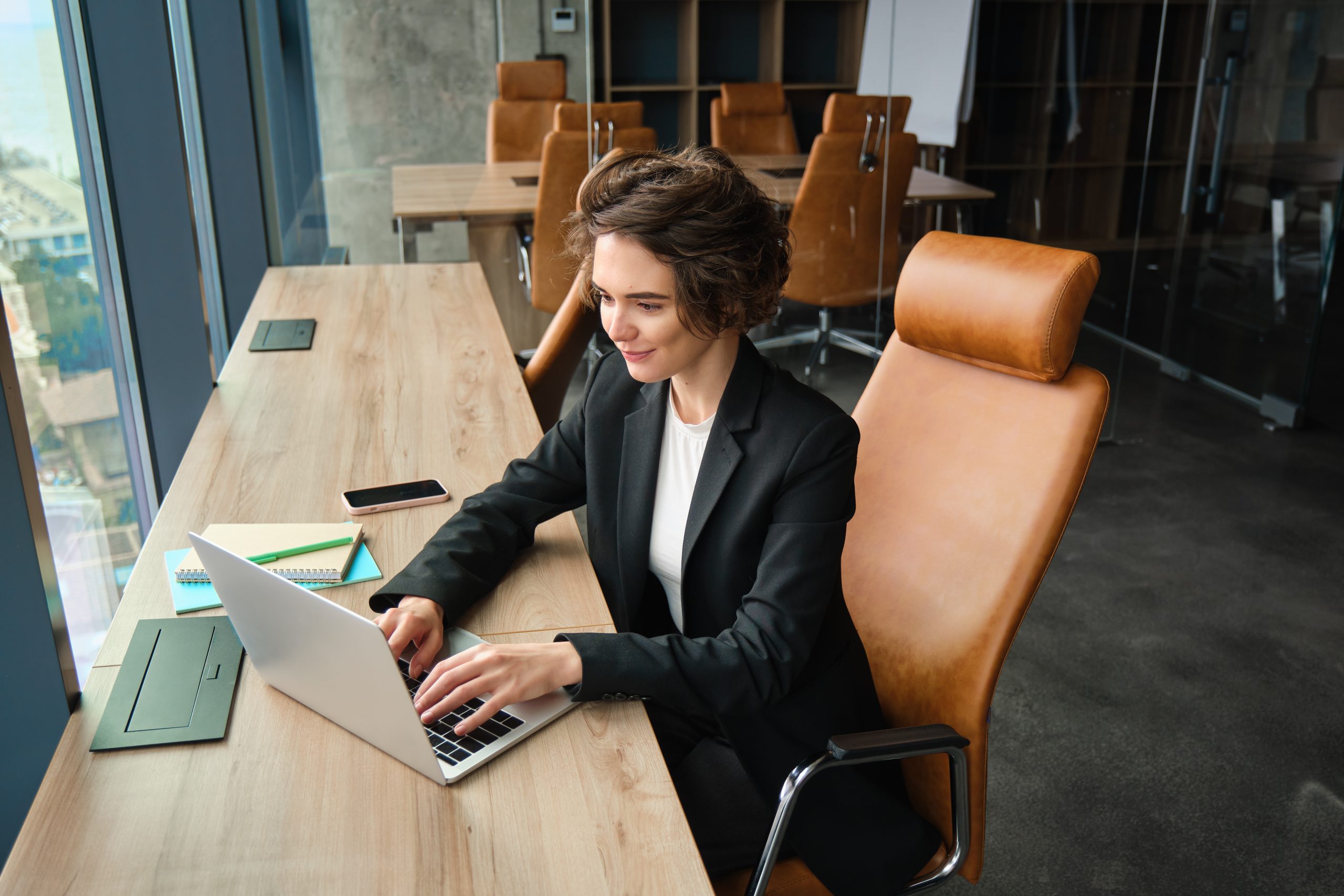 Young female entrepreneur working in her office, using laptop, typing, preparing for a team meeting with business partners, looking professional and confident